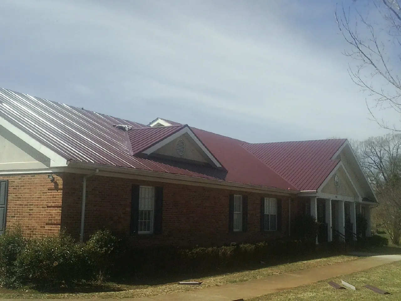Red metal roof with gabled entries on a long brick building, from a Hail Damage Roof Repair job in Acampo
