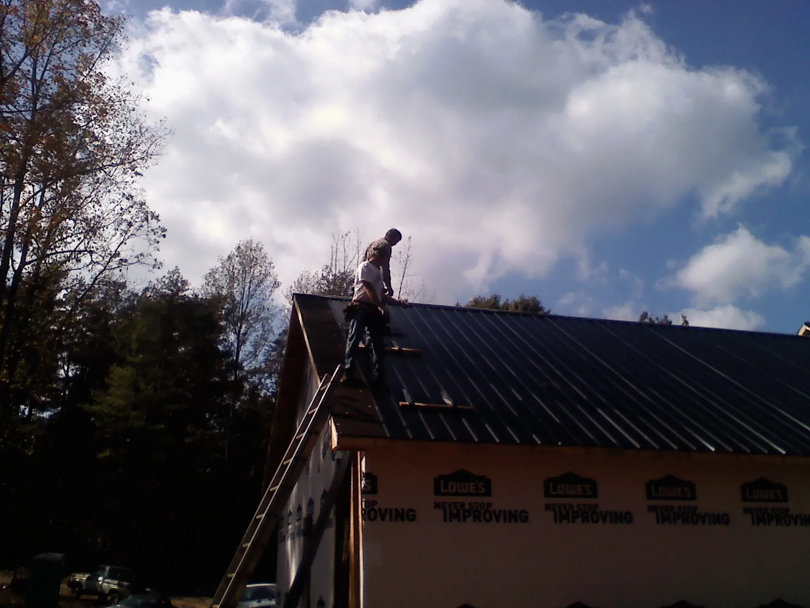 Roofer fastening dark metal panels high against a cloudy sky, from a Roof Inspection job in Acampo